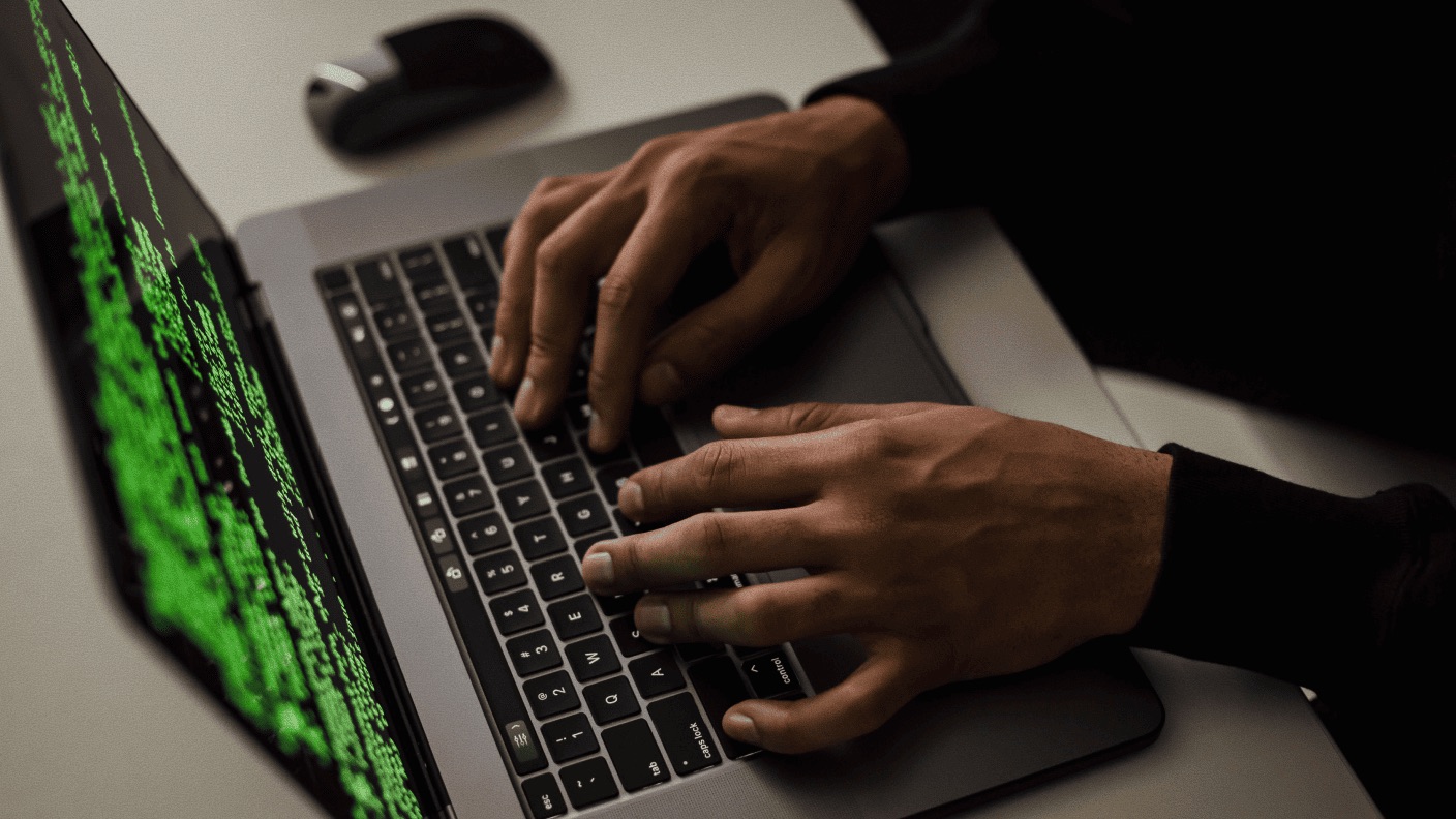 Someone typing on a macbook whose screen is showing green text on a black background.